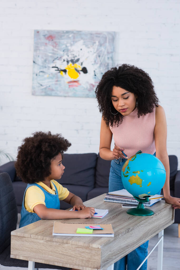 afroamericano madre indicando globo vicino figlia con notebook  - Foto, immagini