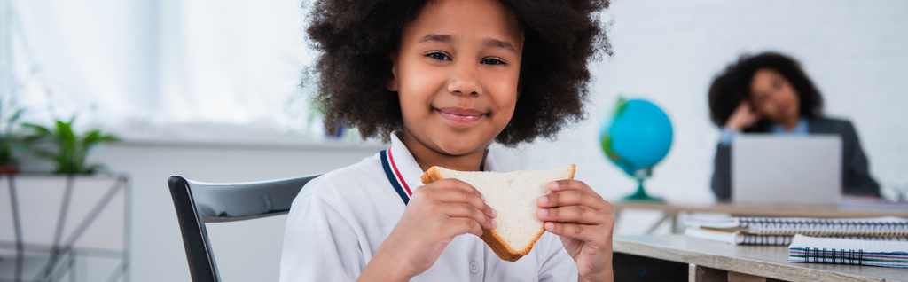 Африканская американская школьница держит сэндвич во время перерыва в классе, баннер  - Фото, изображение