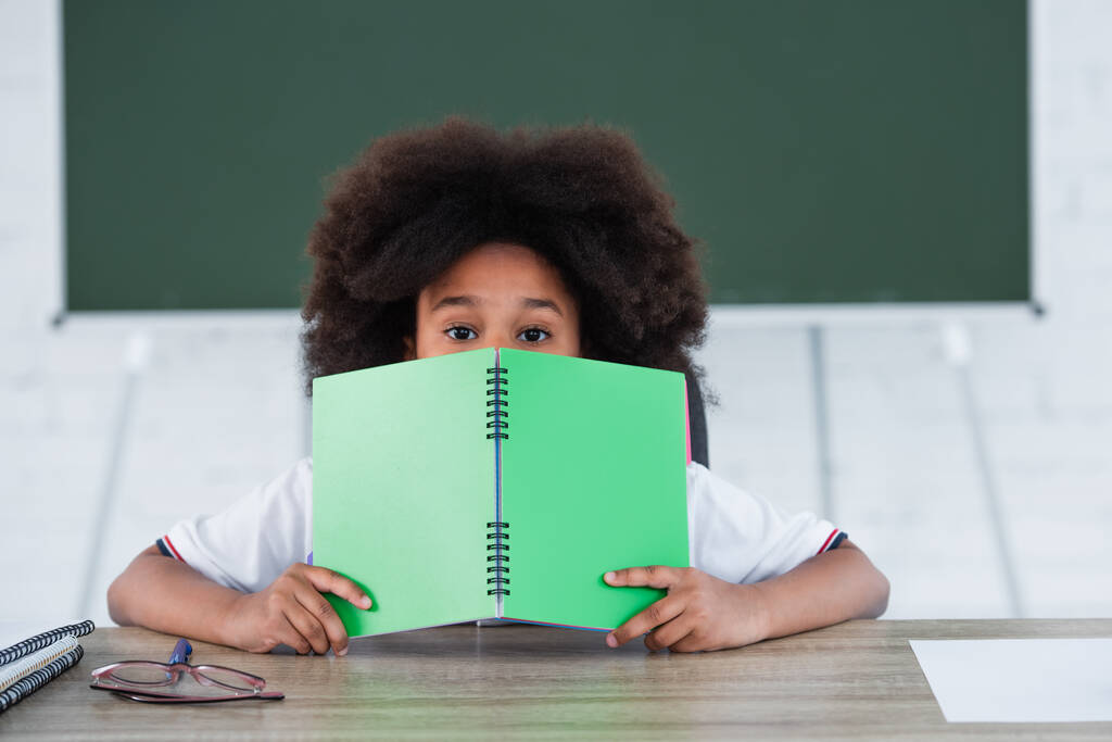 Afrikai amerikai gyerek borító arc könyvvel az osztályteremben  - Fotó, kép