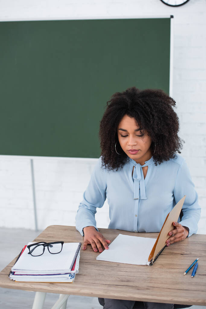 Professor afro-americano olhando para notebook perto de óculos em sala de aula  - Foto, Imagem