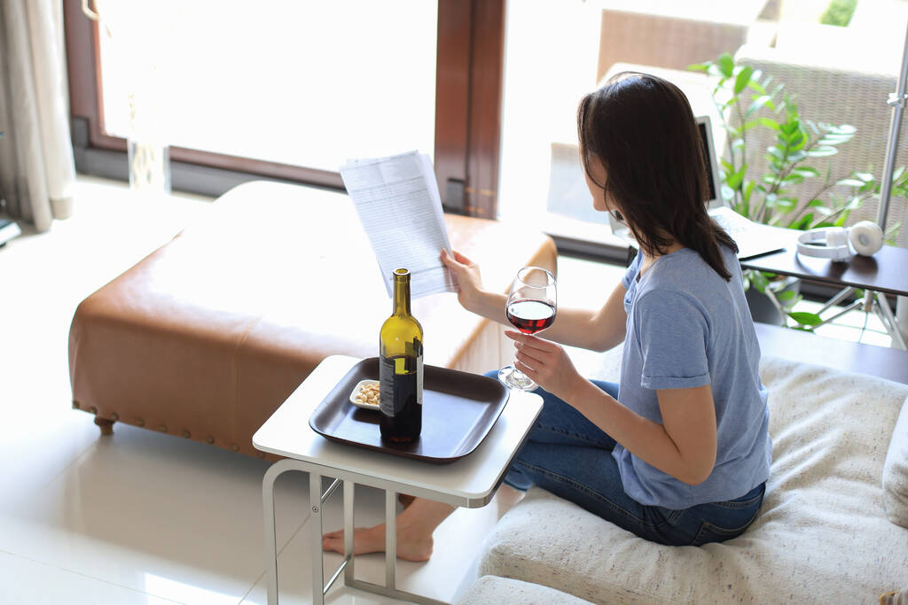 Udane młoda piękna kobieta siedzi na kanapie w salonie, pije czerwone wino, czyta dokumenty - Zdjęcie, obraz