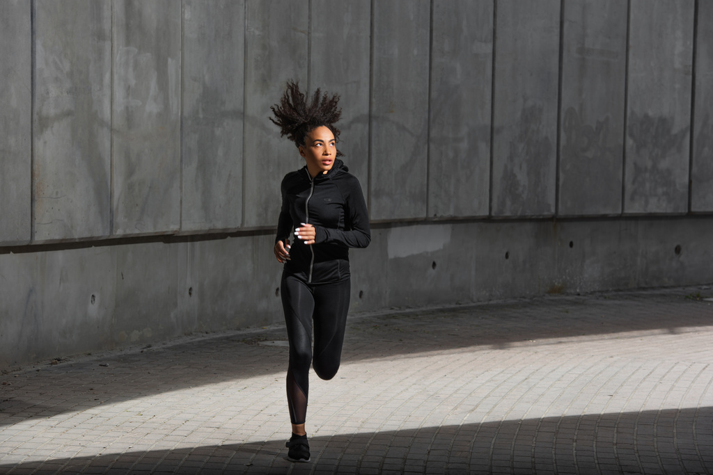 Junge afrikanisch-amerikanische Sportlerin läuft in der Nähe eines Gebäudes auf der Stadtstraße  - Foto, Bild