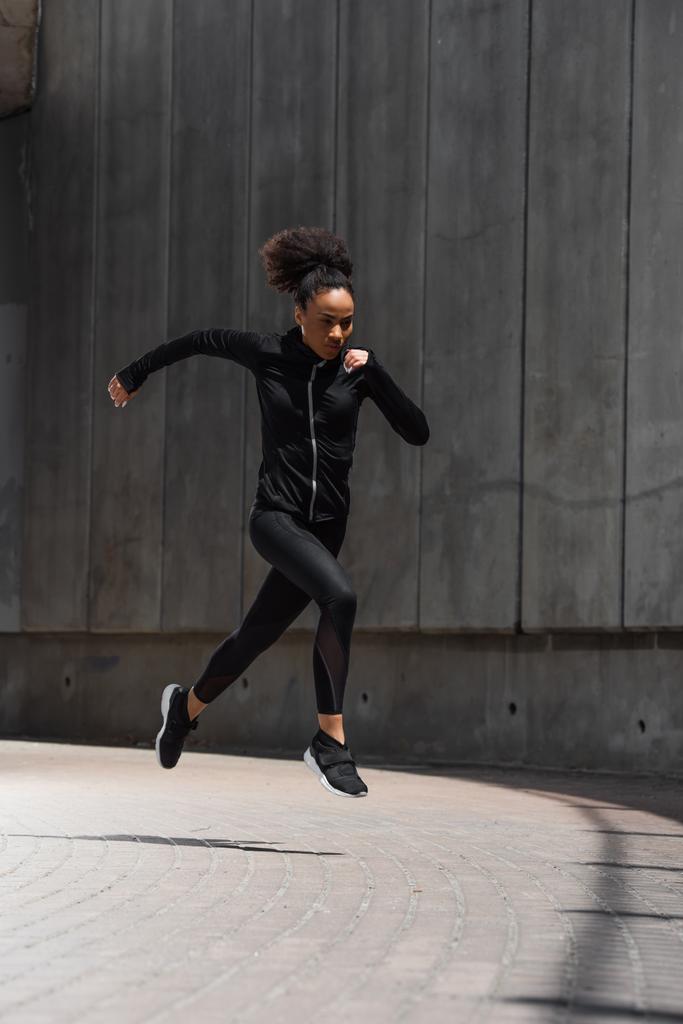 Afrikkalainen amerikkalainen juoksija mustissa urheiluvaatteissa juoksee ulkona  - Valokuva, kuva