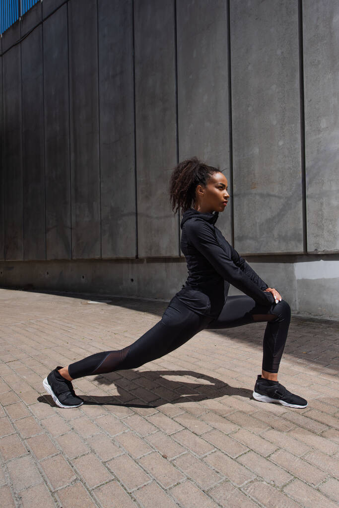 Zijaanzicht van Afro-Amerikaanse sportvrouw stretching benen buiten  - Foto, afbeelding