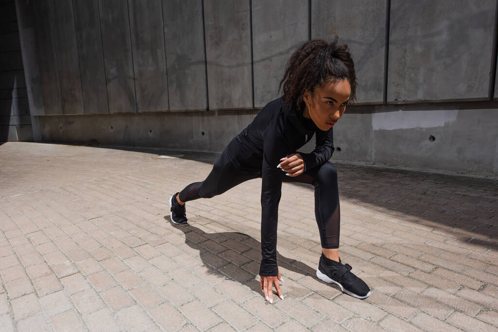 Corredor afroamericano de pie en la postura inicial en la calle urbana  - Foto, Imagen
