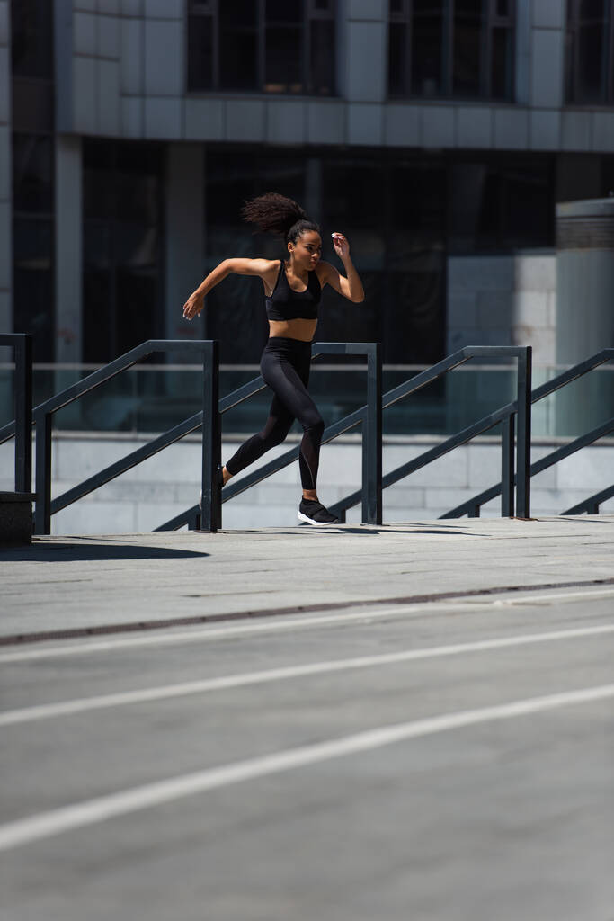 Deportista afroamericana corriendo cerca de barandilla en calle urbana   - Foto, imagen