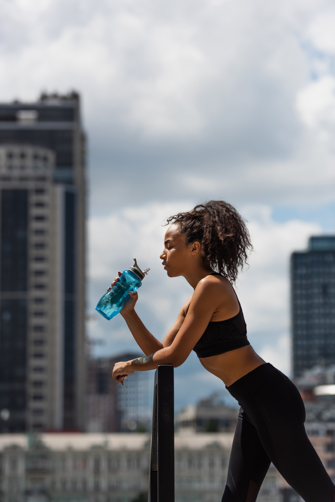 Boční pohled na africké americké sportovkyně pitné vody na městské ulici  - Fotografie, Obrázek