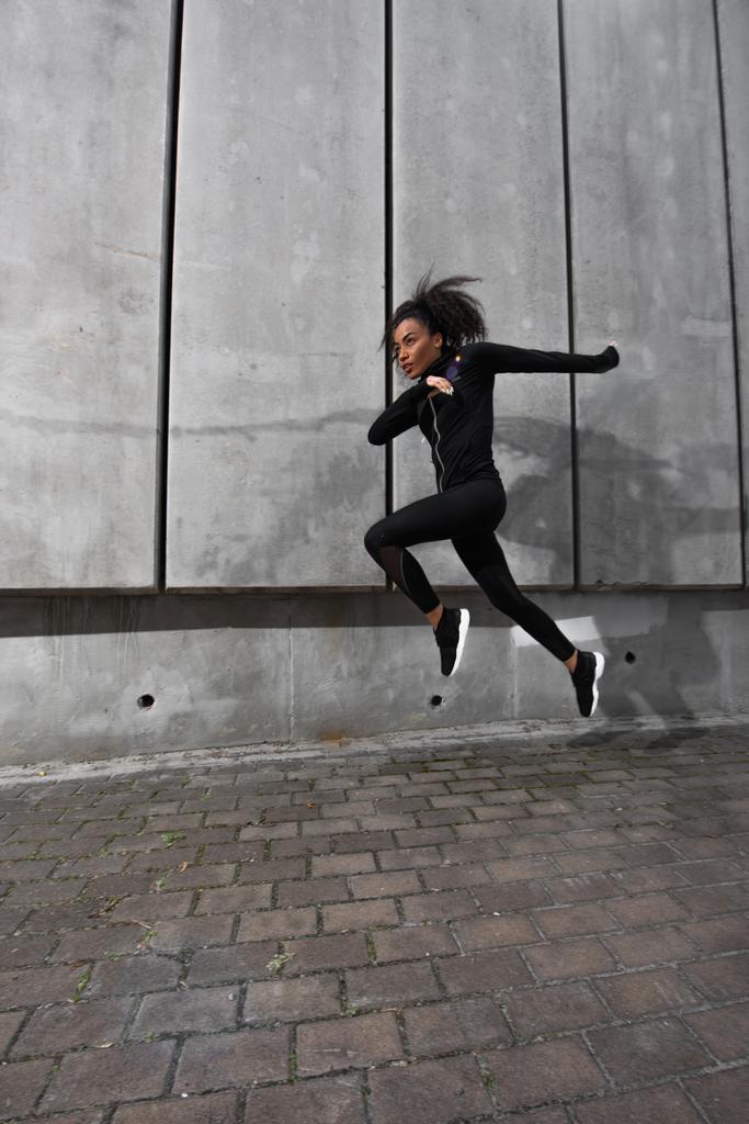Afrikai-amerikai sportos nő fekete sportruházat fut közel beton fal  - Fotó, kép