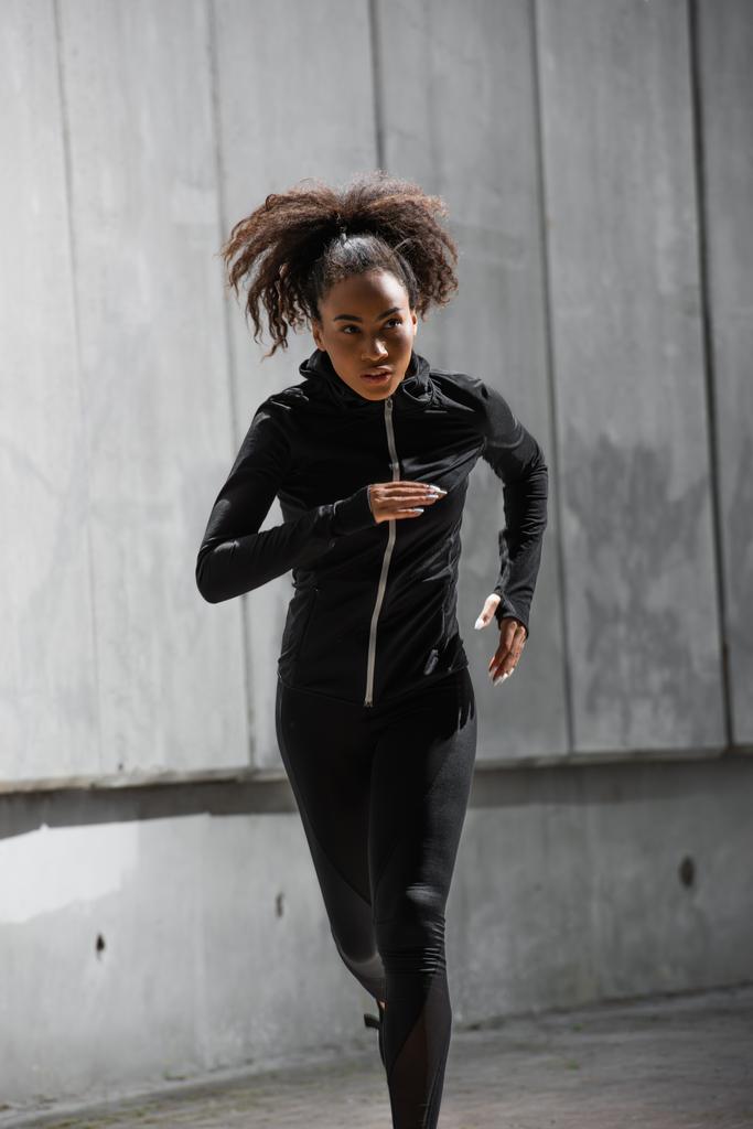 African american runner in black sports jacket looking away while running outdoors  - Photo, Image