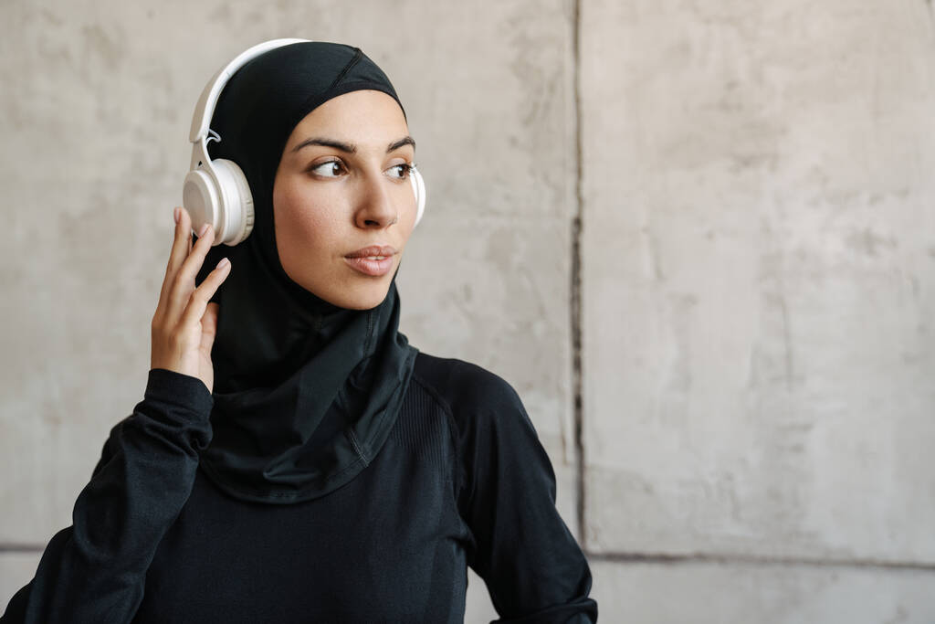Jeune sportive musulmane en hijab écoutant de la musique avec écouteurs à l'intérieur - Photo, image