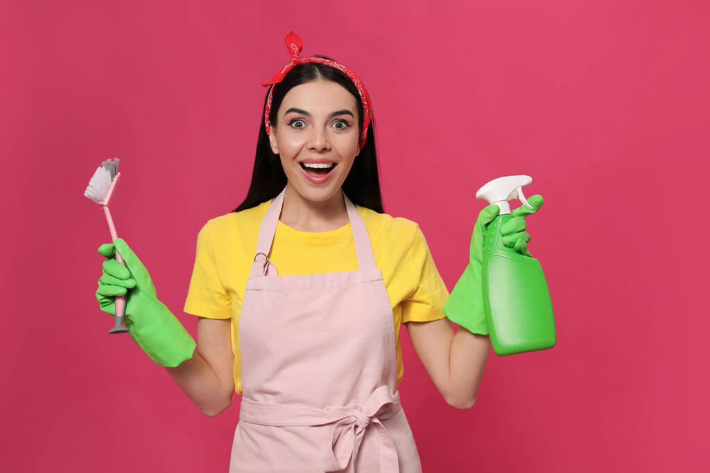 Emocional ama de casa con detergente y cepillo sobre fondo rosa - Foto, imagen