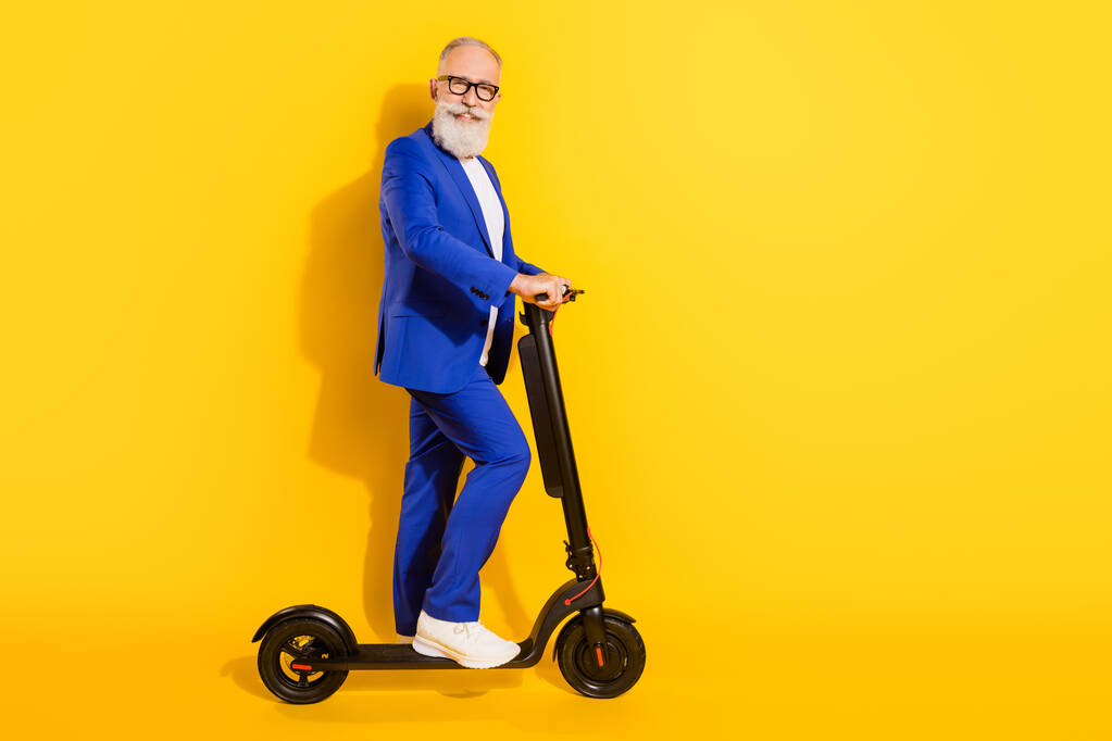Foto de tamaño completo de feliz sonriente buen humor hombre de negocios maduro montar eco scooter aislado en el fondo de color amarillo - Foto, Imagen