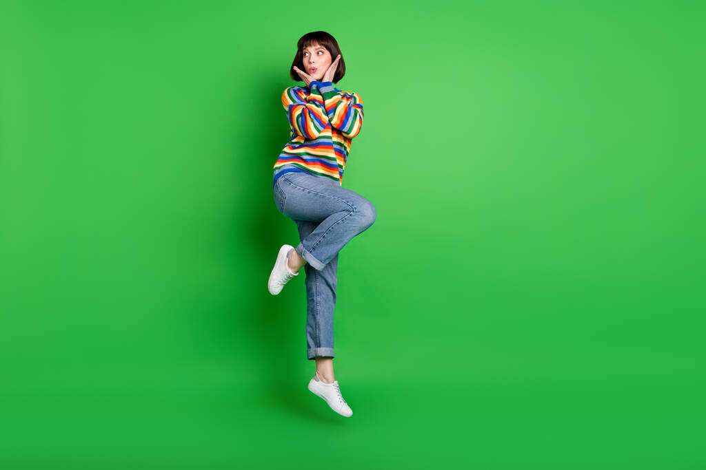 Foto de cuerpo entero de mujer bastante impresionada usar suéter saltando las mejillas de los brazos altos espacio vacío aislado color verde fondo - Foto, imagen
