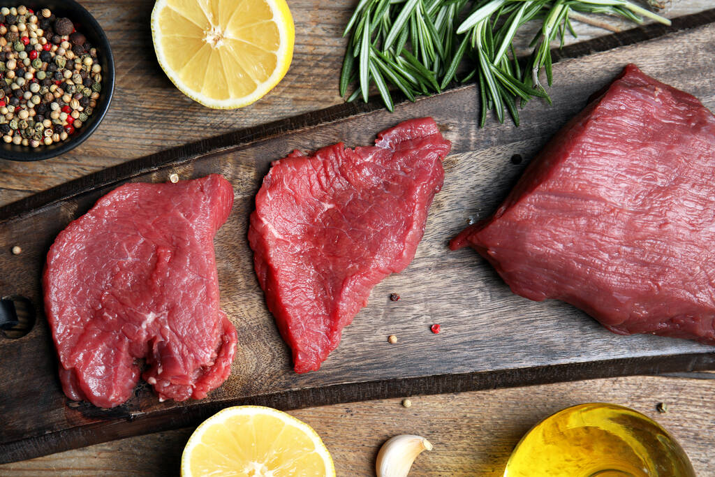 Fresh raw meat steaks and spices on wooden table, flat lay - Photo, Image
