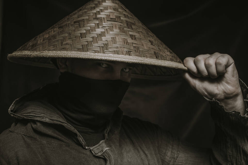 Ninja στο καπέλο θέτει πάνω από σκούρο φόντο - Φωτογραφία, εικόνα
