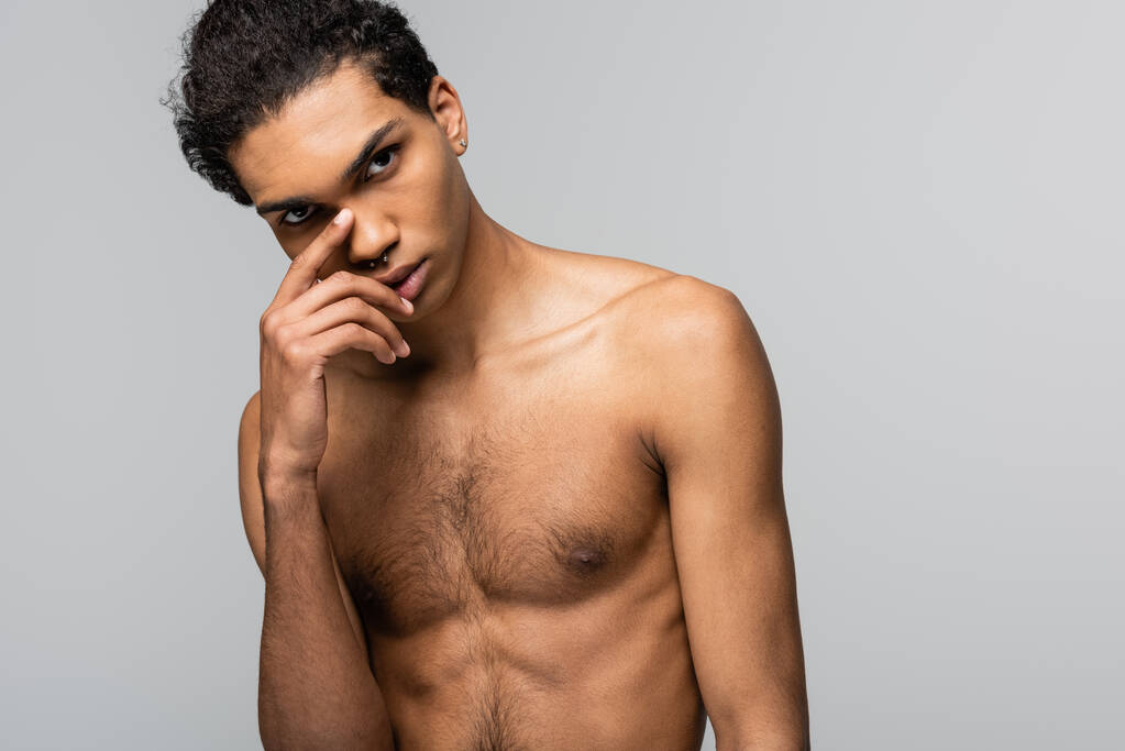 joven, hombre afroamericano sin camisa de pie con la mano cerca de la cara aislado en gris, concepto de belleza - Foto, imagen