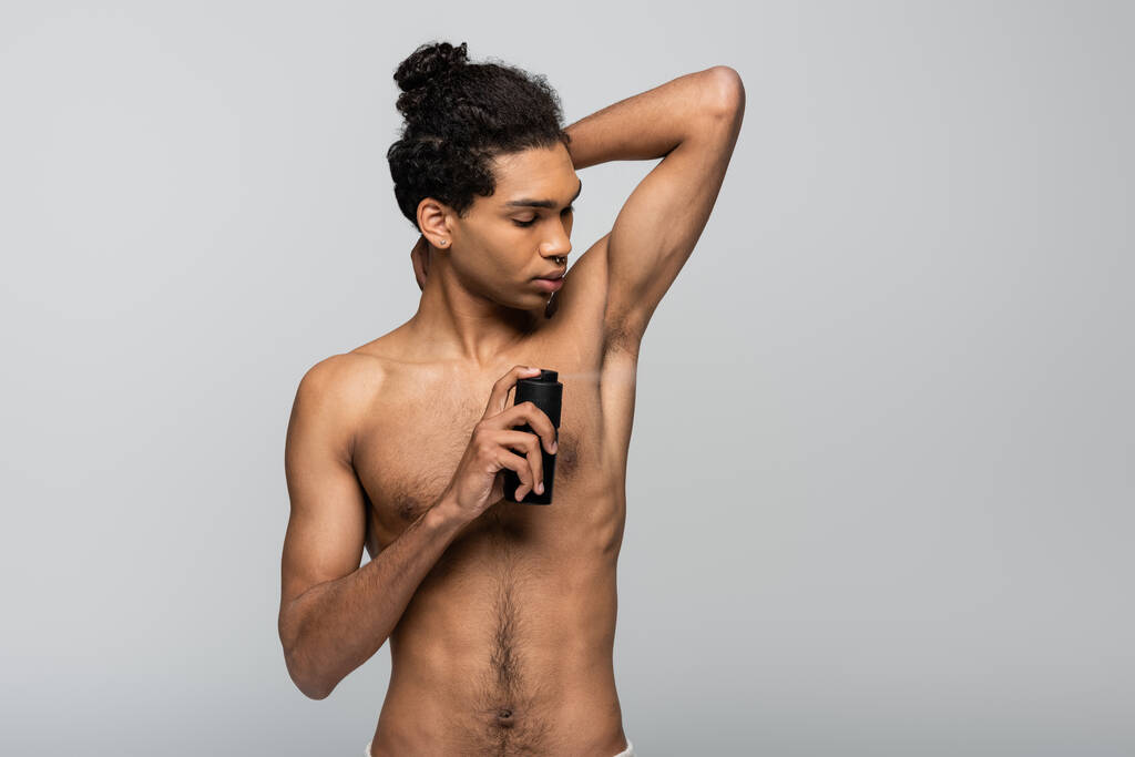paidaton, nuori afrikkalainen amerikkalainen mies ruiskuttamalla antiperspirantti eristetty harmaa - Valokuva, kuva