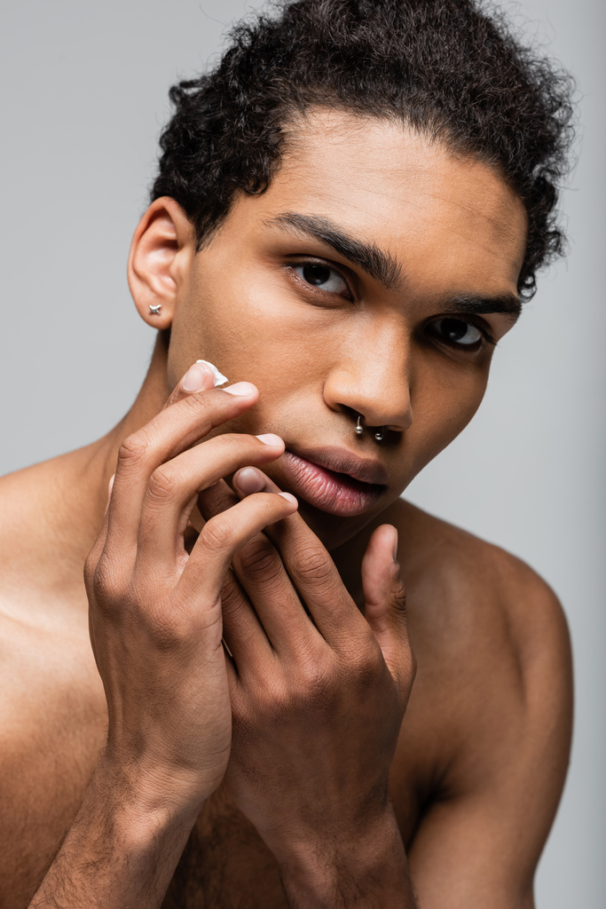 灰色に隔離された顔クリームを適用するアフリカ系アメリカ人男性のピアス ロイヤリティフリー写真 画像素材