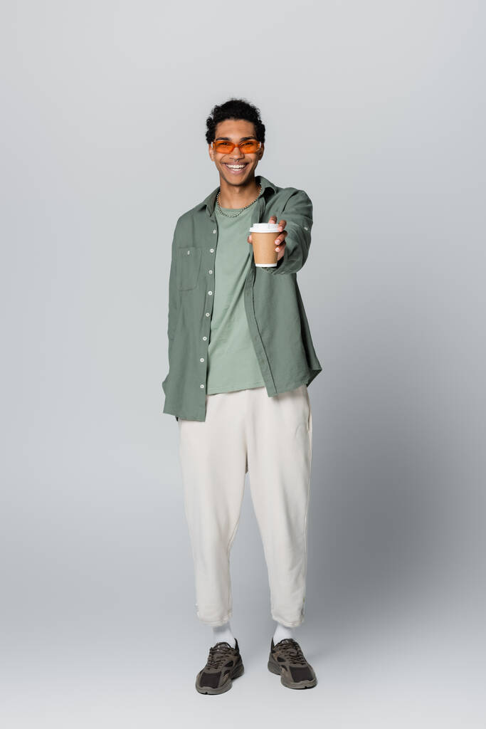 вид на повну довжину молодого афроамериканця, який тримає каву, щоб увійти в простягнуту руку ізольовано на сірому
 - Фото, зображення