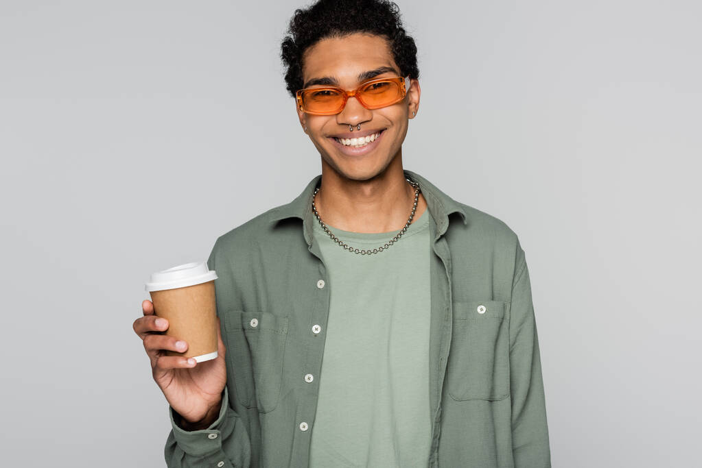 スタイリッシュで幸せなアフリカ系アメリカ人男性コーヒーを飲みながらグレー島のカメラで笑顔になる - 写真・画像