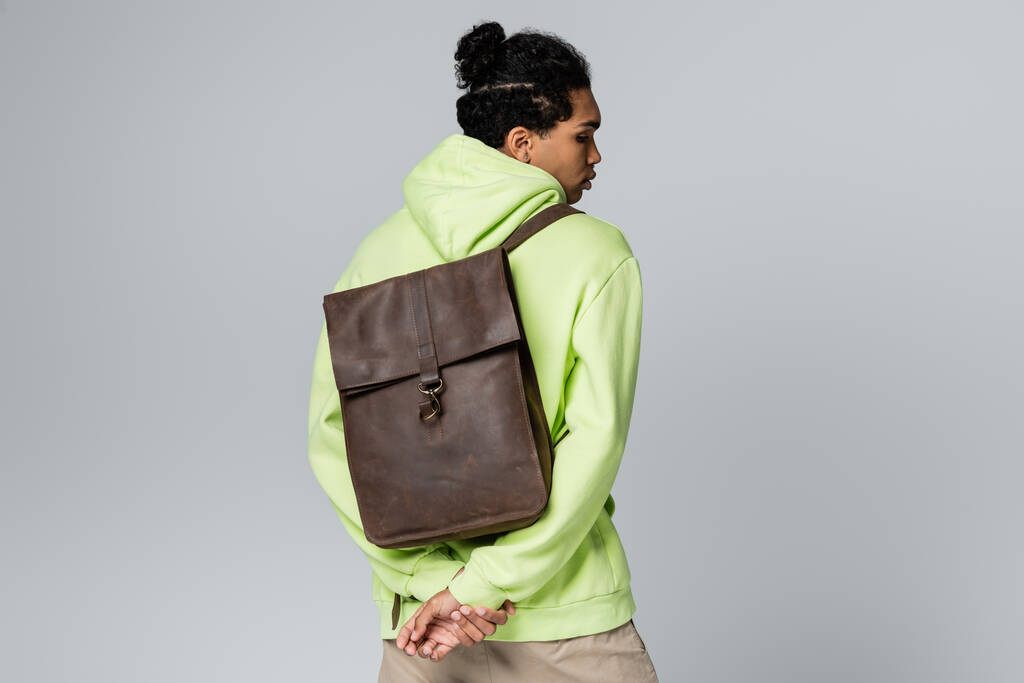 africký Američan v zelené mikině nesoucí kožený batoh izolovaný na šedé - Fotografie, Obrázek