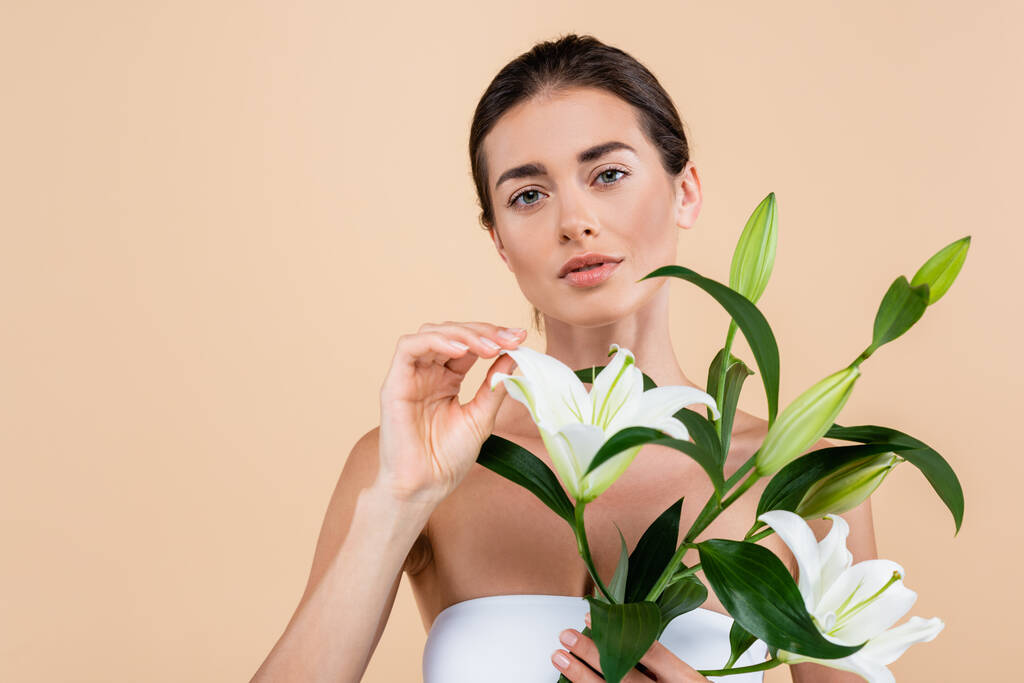 brunette woman with white lily flowers looking at camera isolated on beige, beauty concept - Foto, Imagem