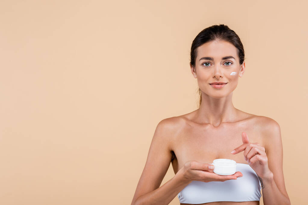 front view of young woman pointing at cosmetic cream container isolated on beige - Foto, Imagem