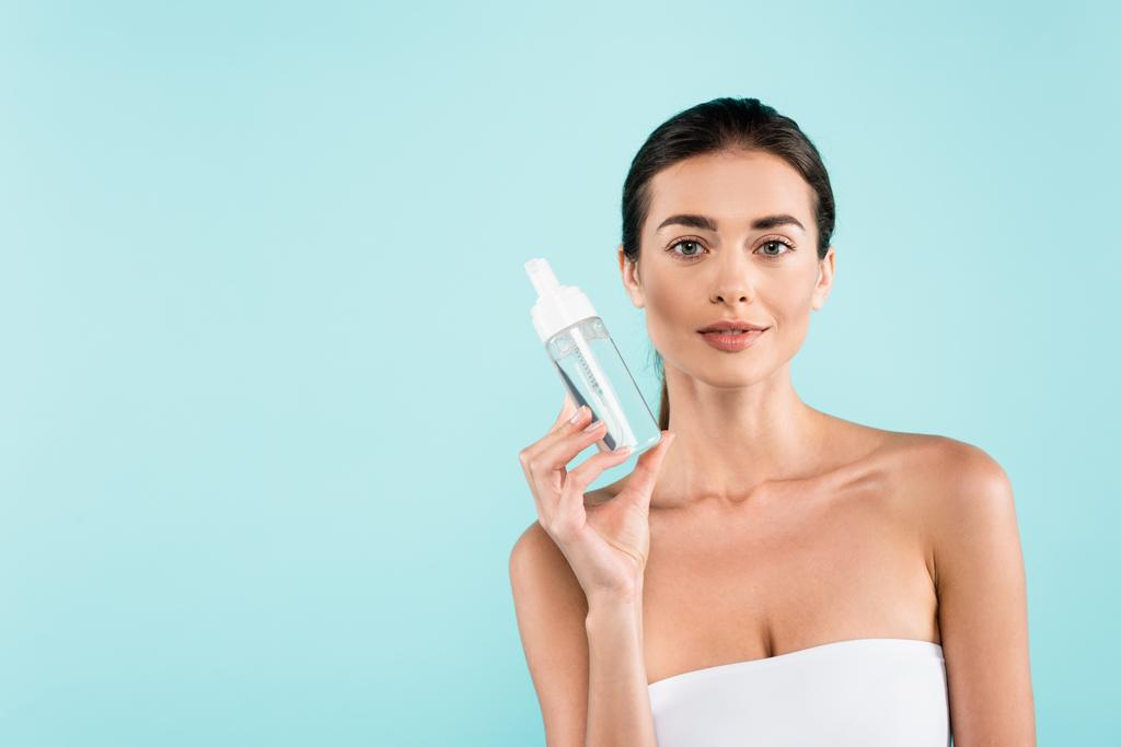 brunette woman in white strapless top showing face tonic isolated on blue - Foto, Imagem