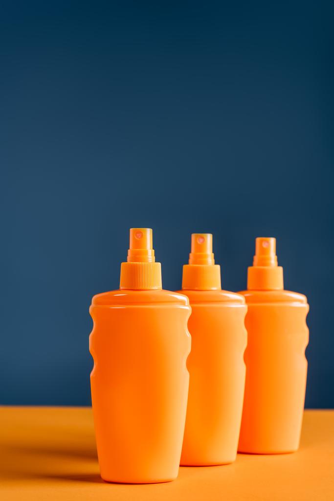 Sprühflaschen mit Sonnencreme auf orangefarbener Oberfläche isoliert auf blauer - Foto, Bild