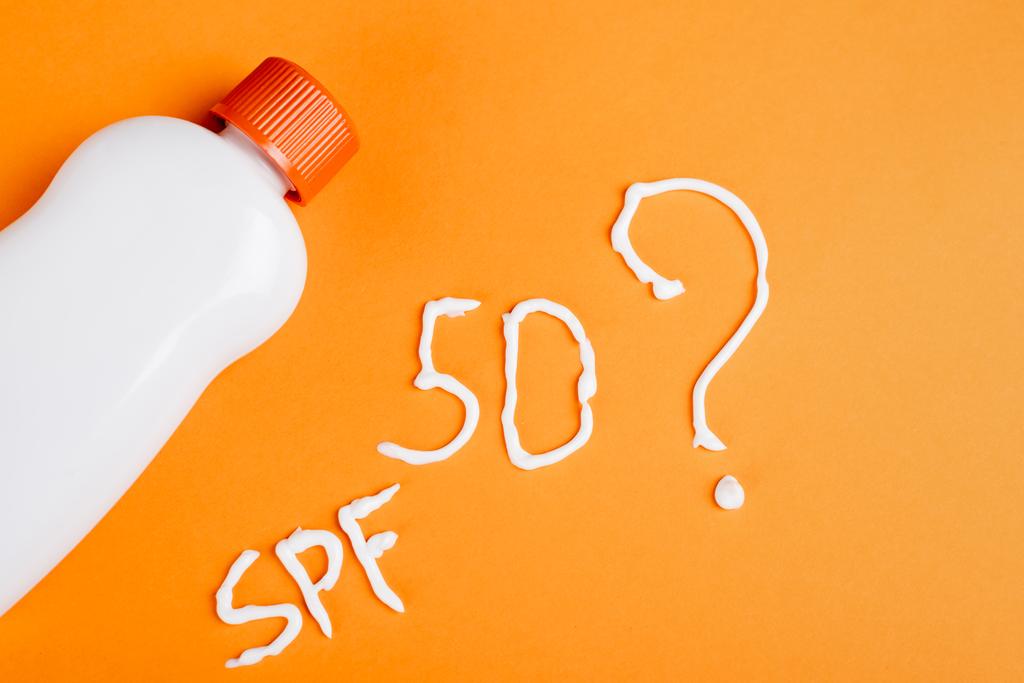 top view of sunscreen near spf lettering, number fifty and question mark on orange background - Photo, Image