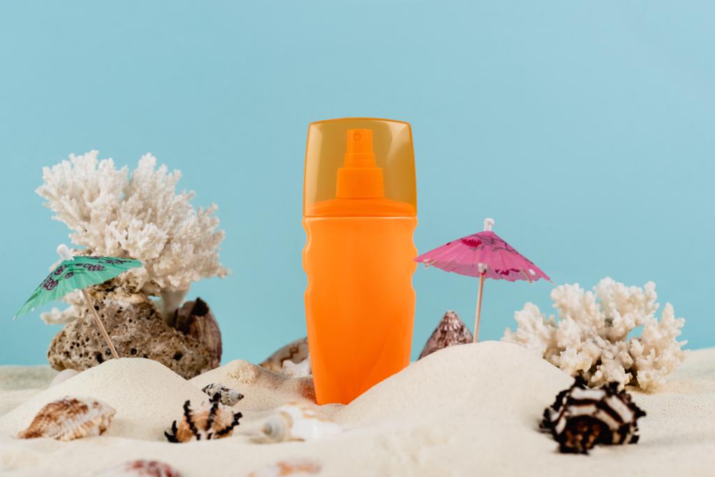pomarańczowa butelka kremu z filtrem przeciwsłonecznym w pobliżu muszli morskich na piasku odizolowanym na niebiesko - Zdjęcie, obraz