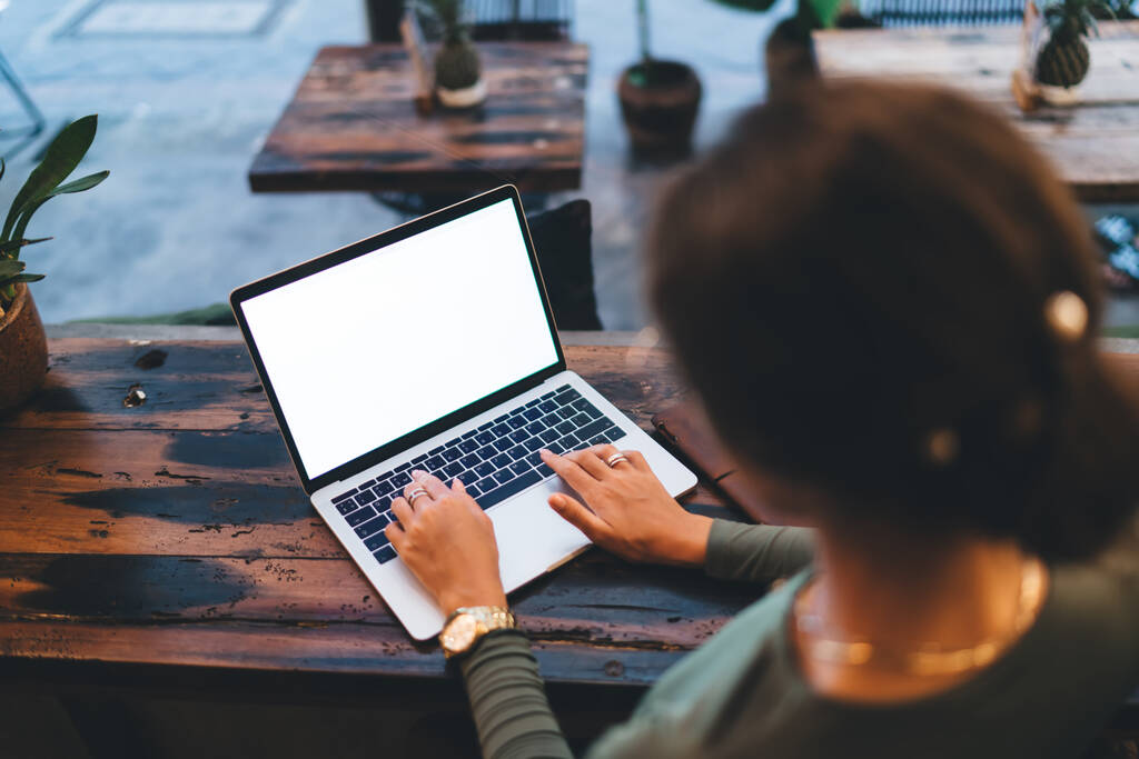 De cima visão traseira de colheita anônima freelancer feminino em roupas casuais trabalhando em laptop com tela em branco no café - Foto, Imagem