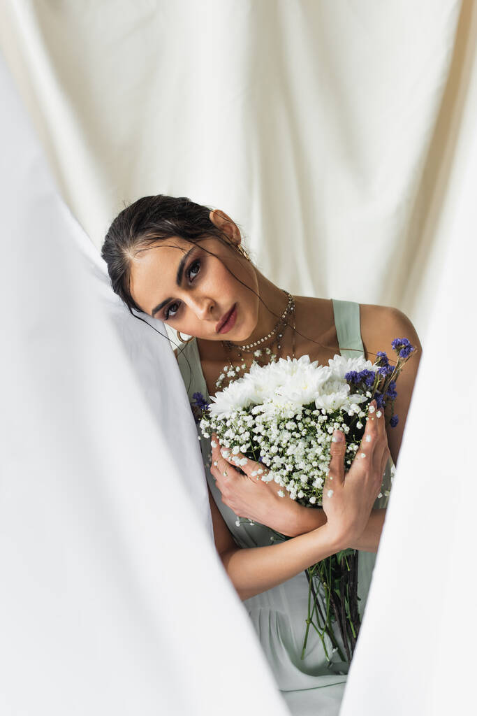 pretty woman looking at camera while holding flowers on white - Photo, Image