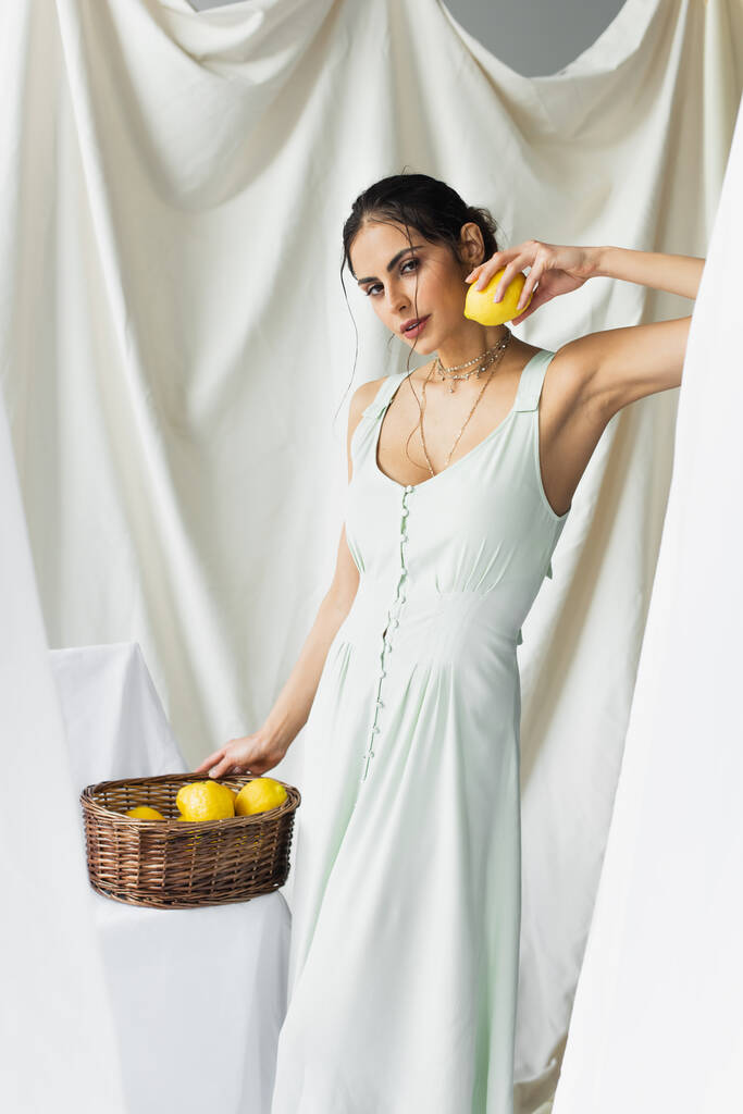 hübsche Frau im Kleid mit reifer Zitrone in der Nähe von Weidenkorb auf weiß - Foto, Bild