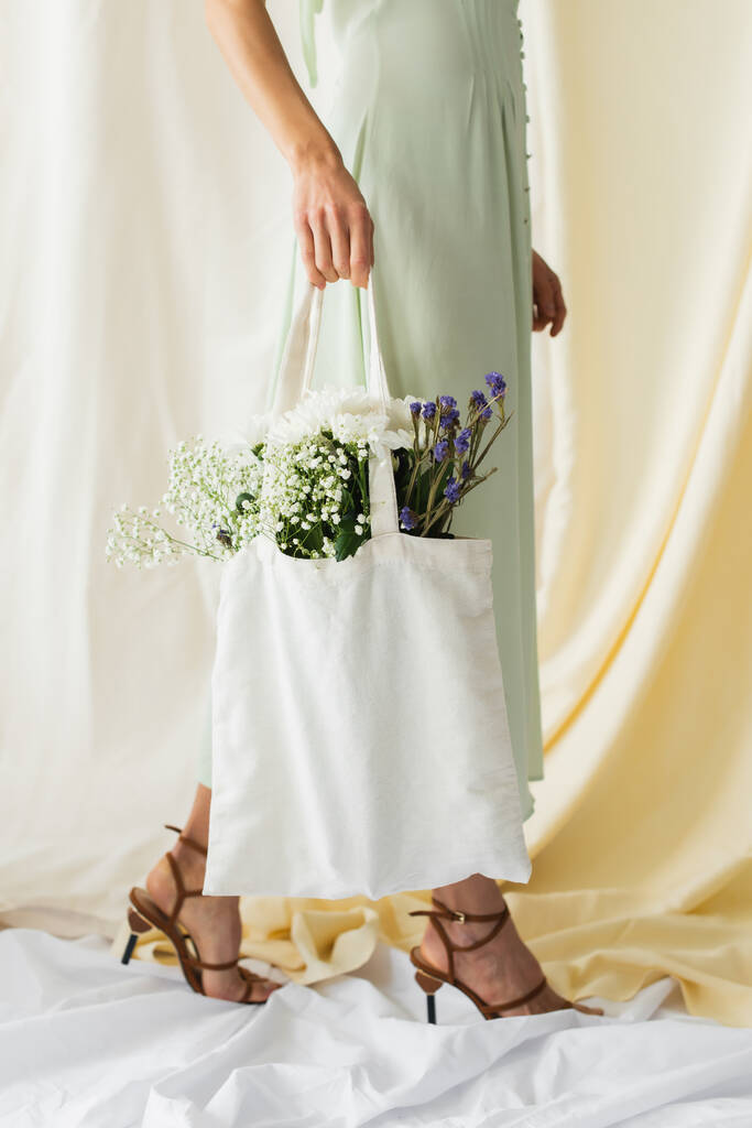 vista recortada de la mujer sosteniendo bolso de comprador de tela con flores y caminando sobre blanco - Foto, imagen