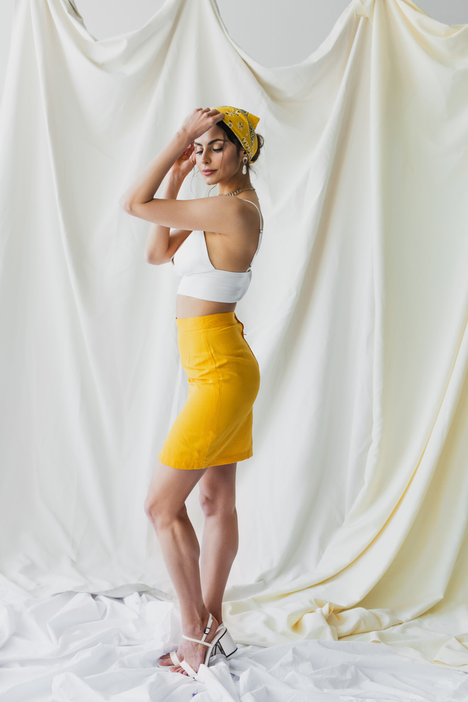 comprimento total da mulher em lenço amarelo, saia e top de cultura posando perto de cortinas brancas - Foto, Imagem