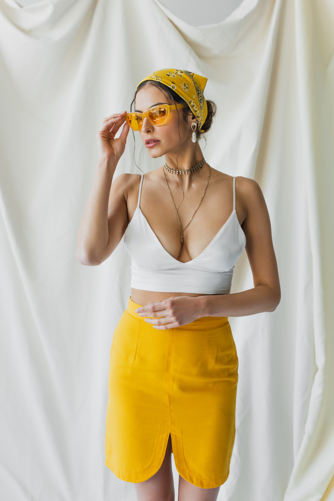 стильная женщина регулирует солнцезащитные очки и позирует на белом - Фото, изображение