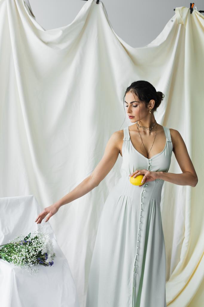 mooie vrouw bereiken bloemen terwijl het houden van verse citroen op wit - Foto, afbeelding
