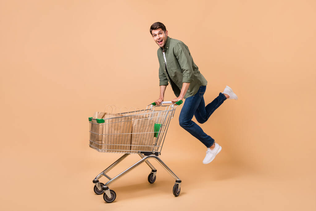 Ganzkörperfoto von attraktiven jungen positiven Mann springen halten Trolley Taschen Geschäft isoliert auf beige Farbhintergrund - Foto, Bild