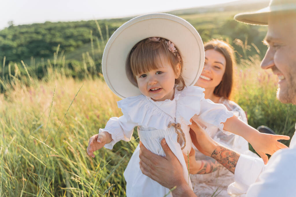 красивая женщина в белом платье с дочкой, сидящей на поле - Фото, изображение