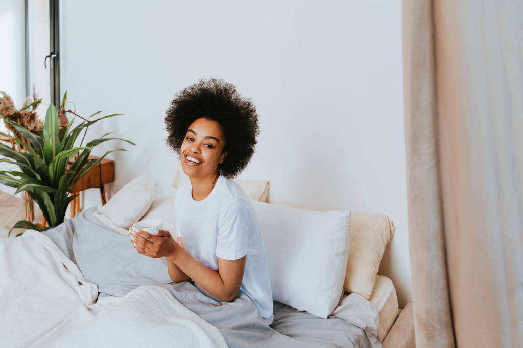 Chica afroamericana descansando en la cama en casa - Hermosa mujer relajándose en casa desayunando en la cama - Foto, Imagen