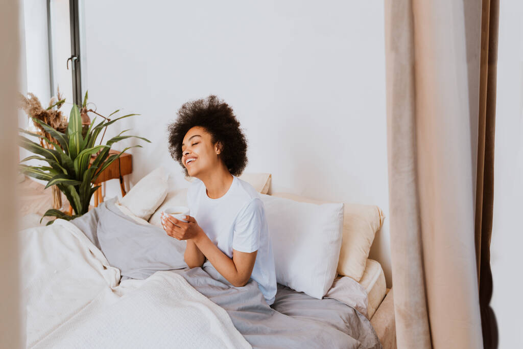 Ragazza afro-americana che riposa a letto a casa - Bella donna che si rilassa a casa facendo colazione a letto - Foto, immagini