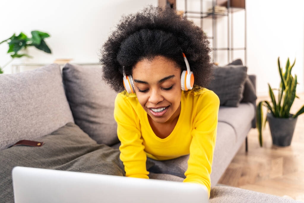 Красивая черная взрослая женщина дома слушает музыку онлайн с ноутбуком и наушниками - Красивая черная девушка работает в удаленном онлайн дома - Фото, изображение
