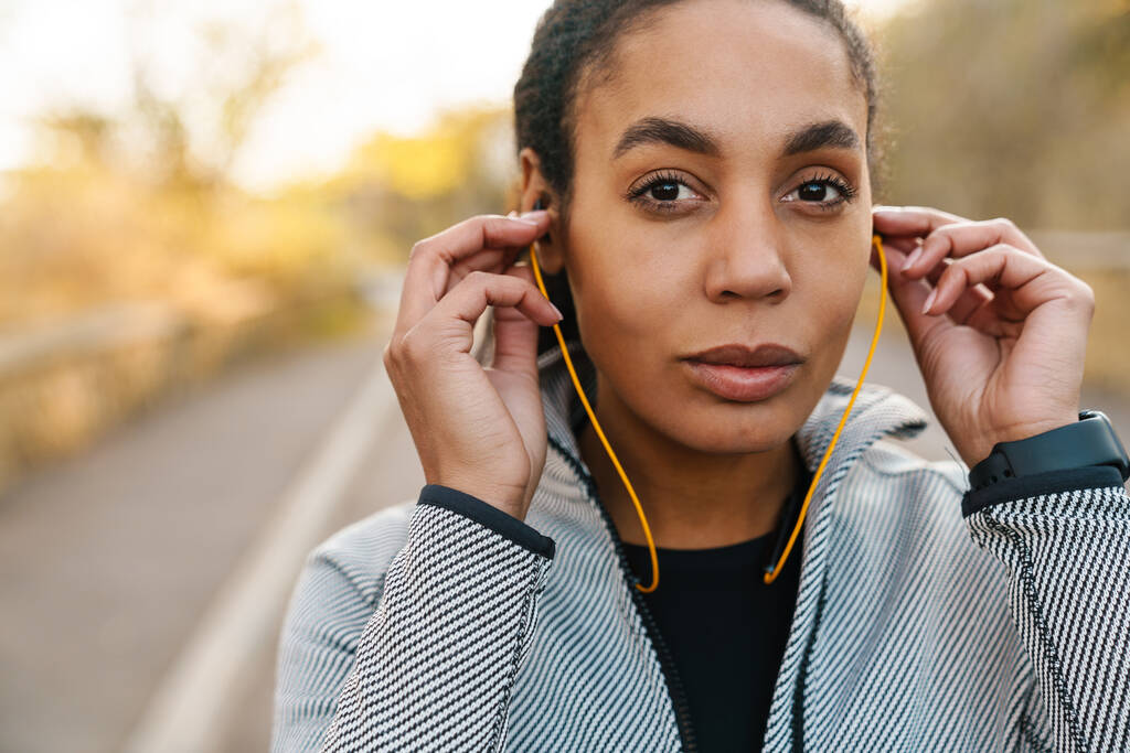 Όμορφη Αφροαμερικανή αθλήτρια που χρησιμοποιεί ακουστικά ενώ γυμνάζεται στο πάρκο - Φωτογραφία, εικόνα