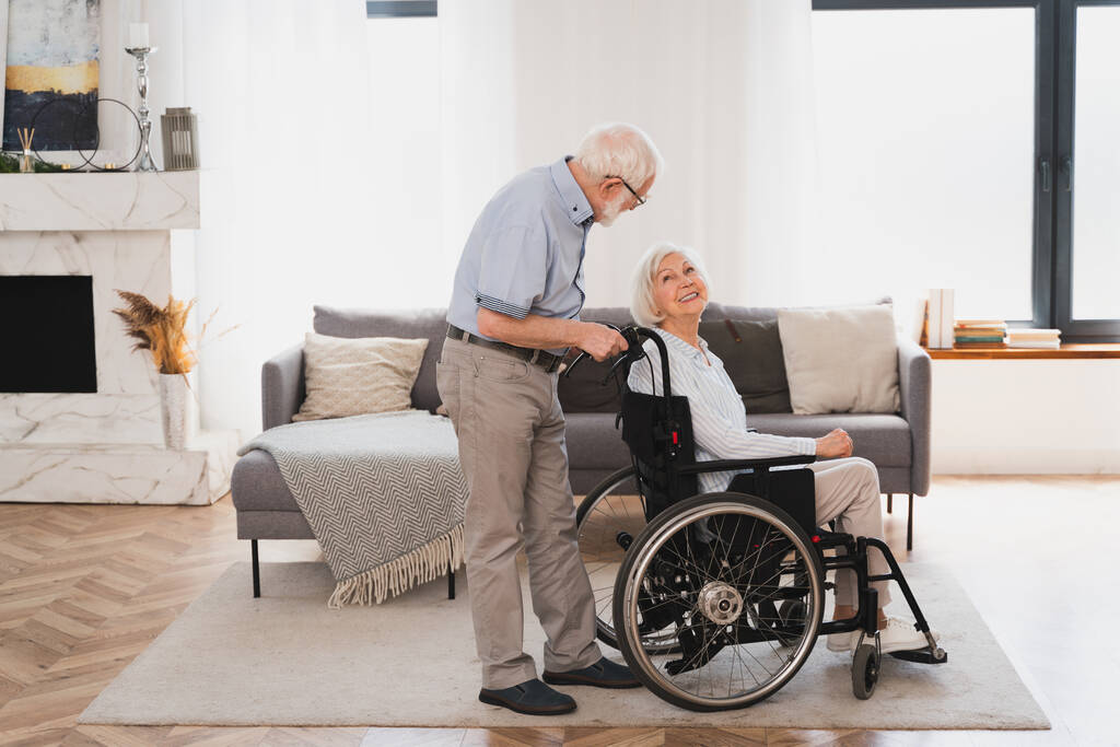 Behinderte alte Frau im Rollstuhl - Seniorenpaar zu Hause, Lebensgefährtin kommt zur Genesung aus Krankenhaus - Foto, Bild