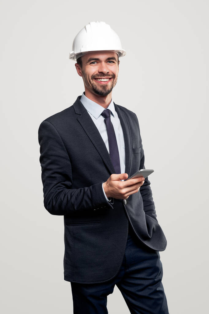 Χαμογελώντας μηχανικός σε hardhat χρησιμοποιώντας smartphone - Φωτογραφία, εικόνα