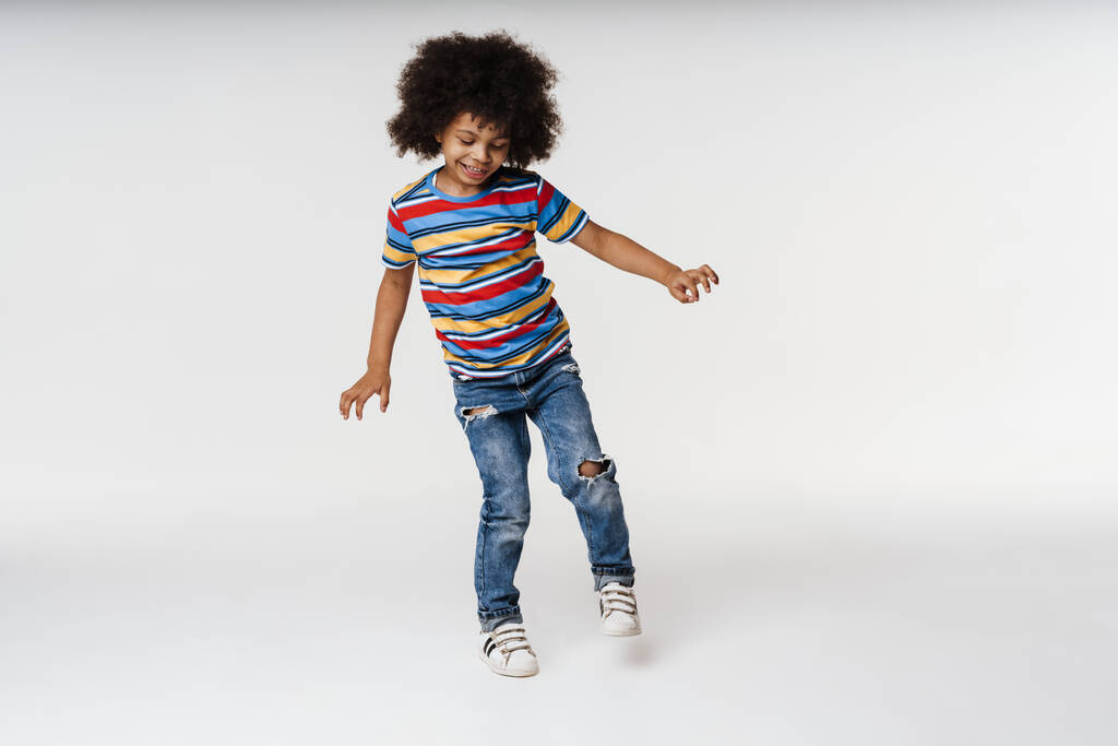 Sonriente niño africano en ropa cotidiana sobre fondo de pared, bailando - Foto, imagen