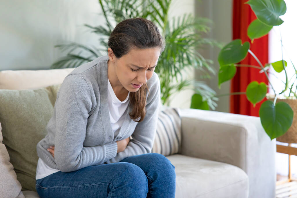 Triste jovem mulher sentada no sofá e sentindo espasmo e sintomas de pms - Foto, Imagem