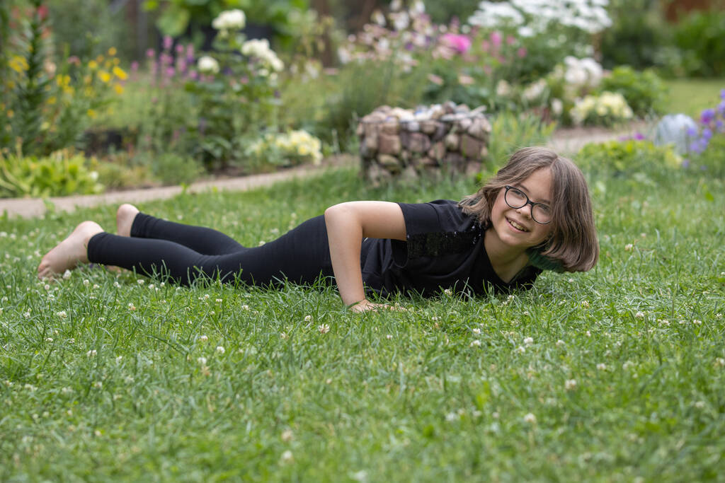 Gözlüklü genç kız yaz bahçesinde çimlere uzanıyor ve gülümsüyor. - Fotoğraf, Görsel