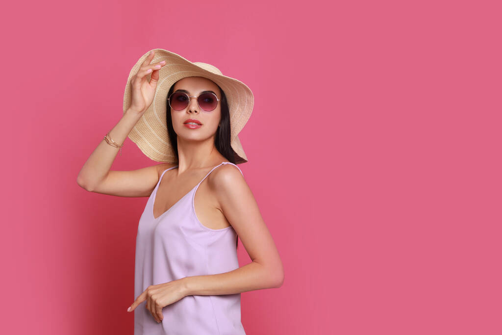 Красивая молодая женщина в соломенной шляпе и стильных солнечных очках на розовом фоне. Пространство для текста - Фото, изображение